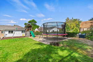 View of grassy yard featuring a trampoline, a playground, and a patio area