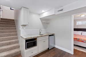 Possible ADU in Basement.  Kitchenette featuring white cabinetry, light stone counters, dark wood-style flooring, stainless steel and black microwave, small fridge and open shelves