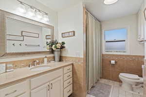 Full bathroom featuring light tile patterned flooring, vanity, tile walls, tub shower with shower curtain, and wainscoting
