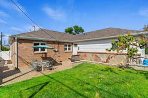 Rear view of house with a yard, a shingled roof, brick siding, and a patio area