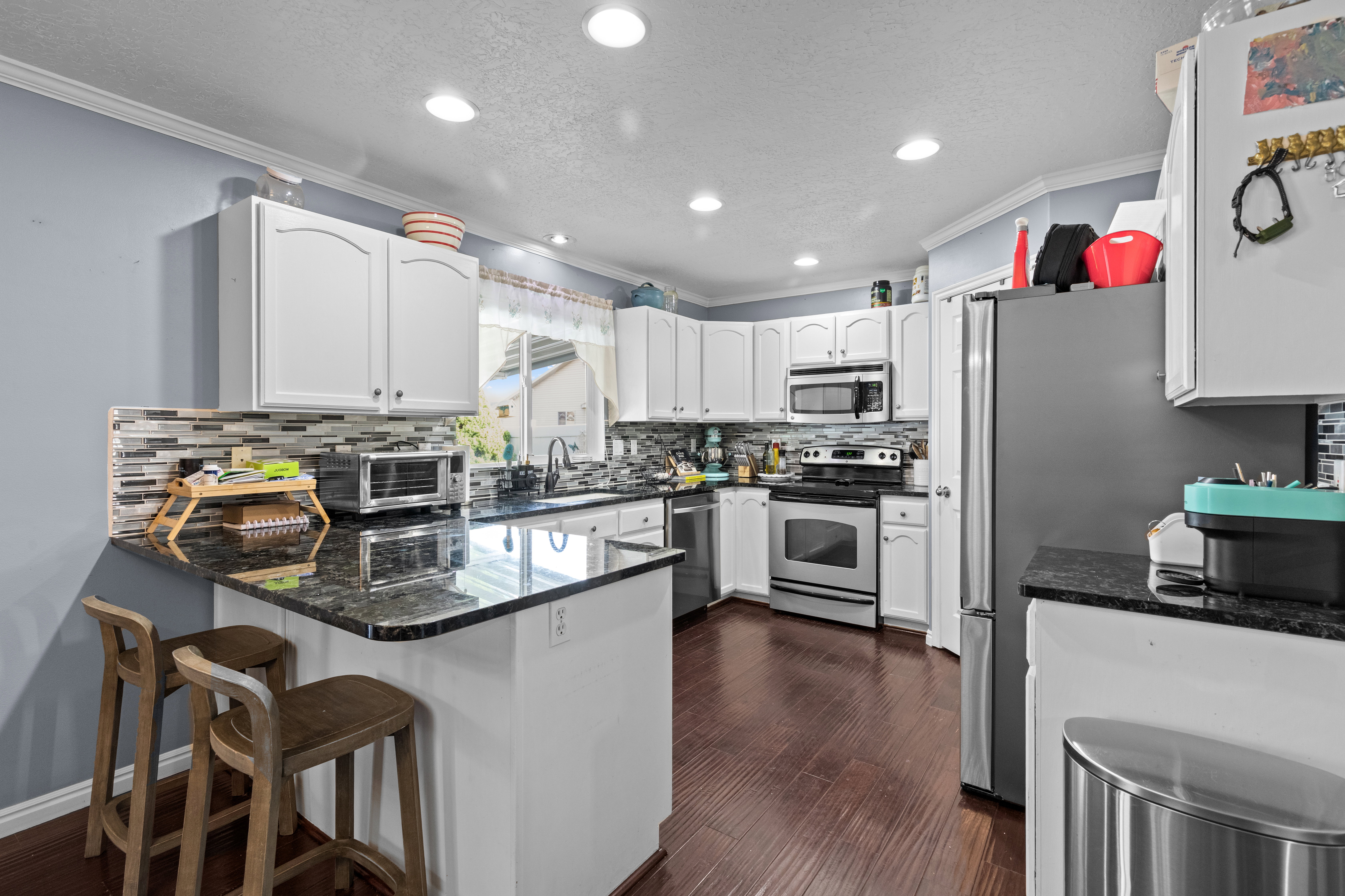 Kitchen with ornamental molding, a peninsula, a textured ceiling, white cabinets, and dark stone countertops