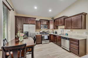 Kitchen featuring appliances with stainless steel finishes, dark brown cabinetry, light wood-type flooring, recessed lighting, and light stone countertops