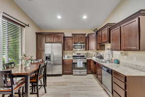 Kitchen with stainless steel appliances, recessed lighting, light wood-style flooring, light stone countertops, and dark brown cabinets