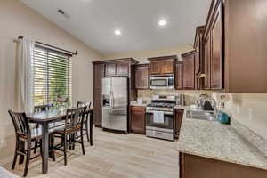 Kitchen featuring stainless steel appliances, recessed lighting, light wood finished floors, light stone countertops, and dark brown cabinetry