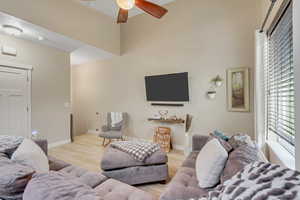 Living room with light wood-style floors, ceiling fan, and a high ceiling