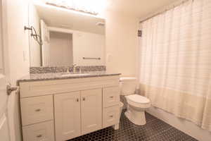 Full bath featuring vanity, dark tile patterned flooring, and shower / tub combo