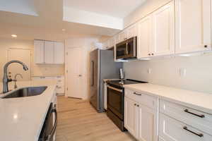 Kitchen with stainless steel appliances, white cabinetry, light wood-style floors, recessed lighting, and light stone counters