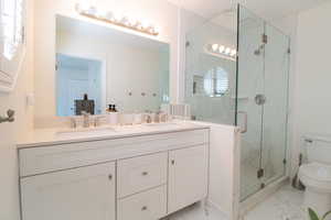 Bathroom with a marble finish shower, double vanity, and light marble finish floors