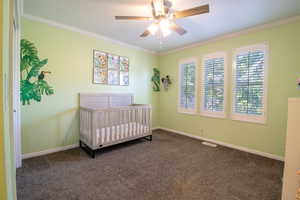 Bedroom featuring a nursery area, ornamental molding, dark colored carpet, and ceiling fan