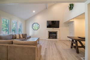 Living area with a premium fireplace, light wood-style floors, high vaulted ceiling, beam ceiling, and recessed lighting