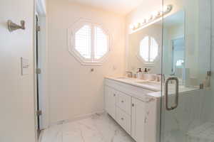 Bathroom with light marble finish flooring, double vanity, healthy amount of natural light, and a marble finish shower