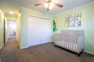Bedroom with a crib, dark carpet, crown molding, a closet, and ceiling fan