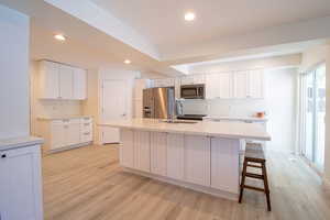 Kitchen with white cabinetry, appliances with stainless steel finishes, recessed lighting, a breakfast bar area, and an island with sink