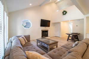 Living room featuring a premium fireplace, beamed ceiling, high vaulted ceiling, light wood-type flooring, and recessed lighting