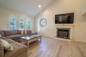Living area with light wood finished floors, high vaulted ceiling, a fireplace, and recessed lighting