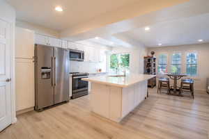 Kitchen with stainless steel appliances, white cabinets, recessed lighting, light wood-type flooring, and a kitchen island with sink