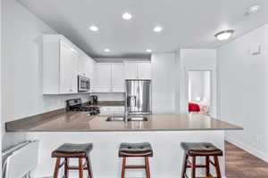 Kitchen featuring a peninsula, white cabinetry, stainless steel appliances, dark wood-style flooring, and dark stone counters
