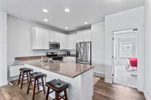 Kitchen featuring white cabinets, stainless steel appliances, a breakfast bar area, a peninsula, and dark stone counters