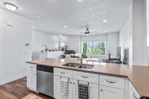 Kitchen featuring light stone counters, stainless steel dishwasher, white cabinets, dark wood-style floors, and open floor plan