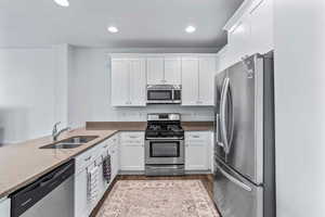 Kitchen featuring stainless steel appliances, white cabinets, dark stone counters, dark wood-type flooring, and recessed lighting