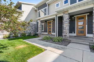 Doorway to property featuring covered porch, stone siding, and a lawn