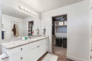 Full bathroom featuring a spacious closet, a textured ceiling, vanity, and dark wood-style flooring