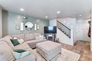 Living room with a textured ceiling, wood finished floors, a fireplace, recessed lighting, and stairway