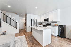 Kitchen featuring white cabinets, stainless steel appliances, dark wood-type flooring, light stone counters, and a textured ceiling
