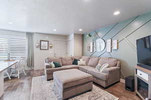 Living area with a textured ceiling, wood-type flooring, and recessed lighting