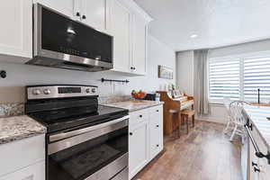 Kitchen with appliances with stainless steel finishes, white cabinetry, light stone countertops, a textured ceiling, and light wood-style floors