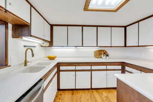 Kitchen featuring white cabinetry, light countertops, brown cabinets, light wood-style floors, and dishwasher