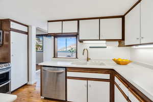 Kitchen with white cabinetry, stainless steel appliances, light countertops, light wood-type flooring, and brown cabinets