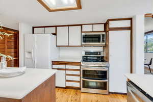 Kitchen with light countertops, stainless steel appliances, white cabinets, and light wood-style flooring