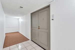Hallway featuring light carpet, a textured ceiling, and light tile patterned floors