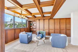 Den featuring coffered ceiling, beamed ceiling, carpet floors, a chandelier, and wood walls