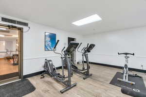 Exercise area with light wood-type flooring and baseboards