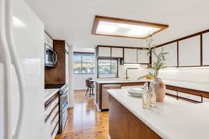 Kitchen with stainless steel appliances, light countertops, brown cabinetry, light wood-style floors, and white cabinetry