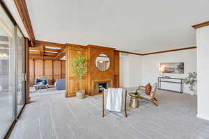 Living area featuring a fireplace, ornamental molding, carpet floors, a textured ceiling, and wooden walls