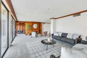 Living area with crown molding, carpet, wooden walls, and a textured ceiling