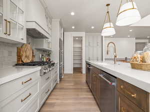 Kitchen featuring glass insert cabinets, appliances with stainless steel finishes, decorative light fixtures, custom exhaust hood, and light wood-style flooring