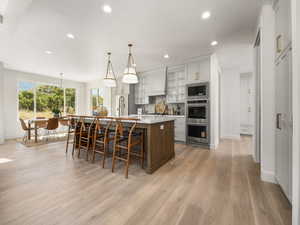 Kitchen with glass insert cabinets, a center island with sink, pendant lighting, recessed lighting, and a breakfast bar
