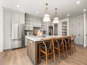 Kitchen with stainless steel appliances, glass insert cabinets, an island with sink, hanging light fixtures, and tasteful backsplash
