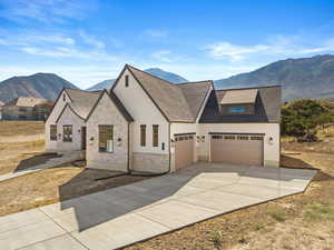 View of front of property with a mountain view, concrete driveway, a shingled roof, stucco siding, and an attached garage
