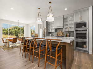 Kitchen featuring tasteful backsplash, a center island with sink, appliances with stainless steel finishes, glass insert cabinets, and dark wood-style floors