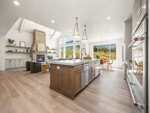 Kitchen with open floor plan, decorative light fixtures, a fireplace, a center island with sink, and recessed lighting