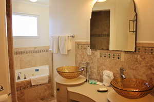 Full bath with a whirlpool tub, crown molding, double vanity, and tile walls