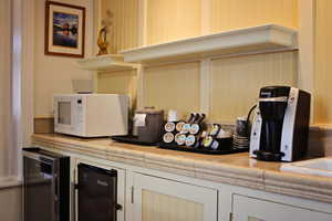 Kitchen view of wine cooler, white microwave, black fridge, and tile countertops