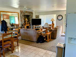 Living room with light colored carpet, a textured ceiling, a ceiling fan, and light tile patterned flooring