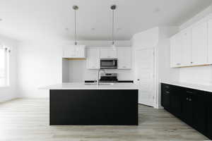 Kitchen with dark cabinets, white cabinets, hanging light fixtures, and a kitchen island with sink