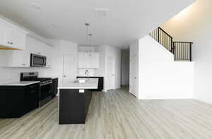 Kitchen featuring dark cabinetry, stainless steel appliances, white cabinets, an island with sink, and light wood-style flooring